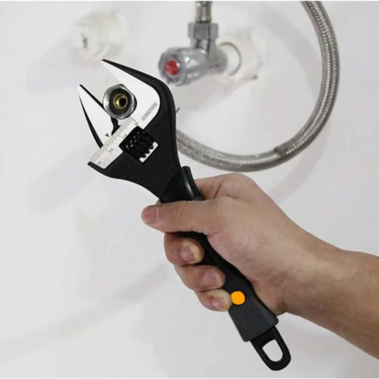 Ruka drži podesivi ključ s mjernom skalom uz fleksibilno crijevo i maticu; univerzalni alat za cijevi, slavine i kućne DIY popravke.