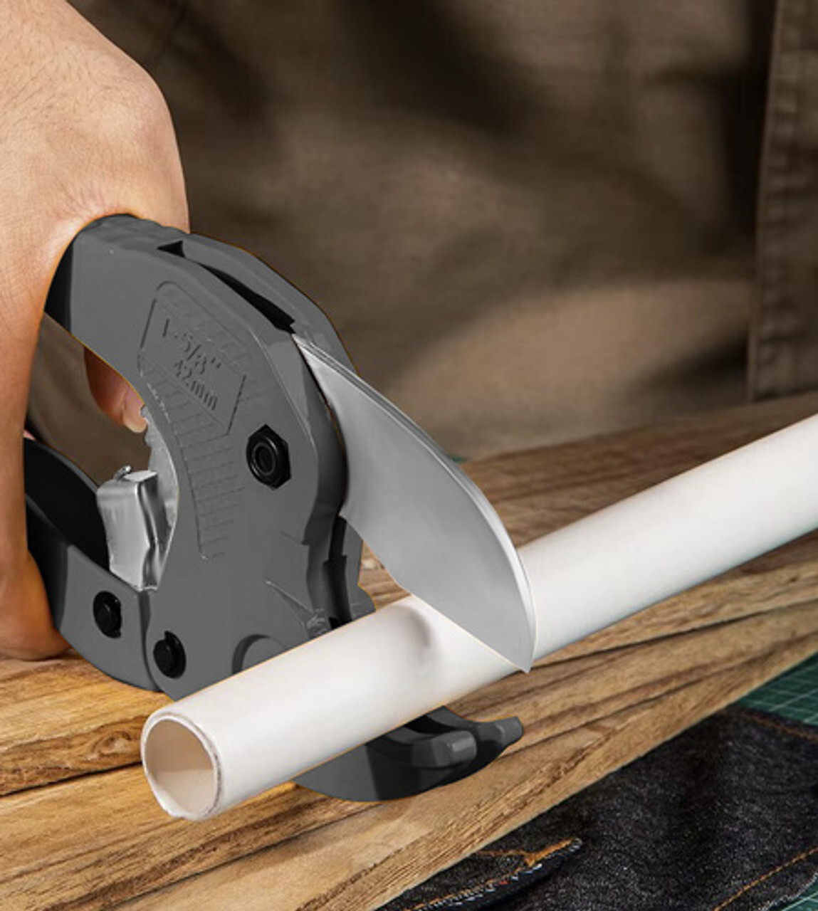 Ručni rezač cijevi reže bijelu PVC/PPR cijev na radnoj podlozi; precizan alat za vodoinstalacije, čiste rezove i DIY kućne popravke.