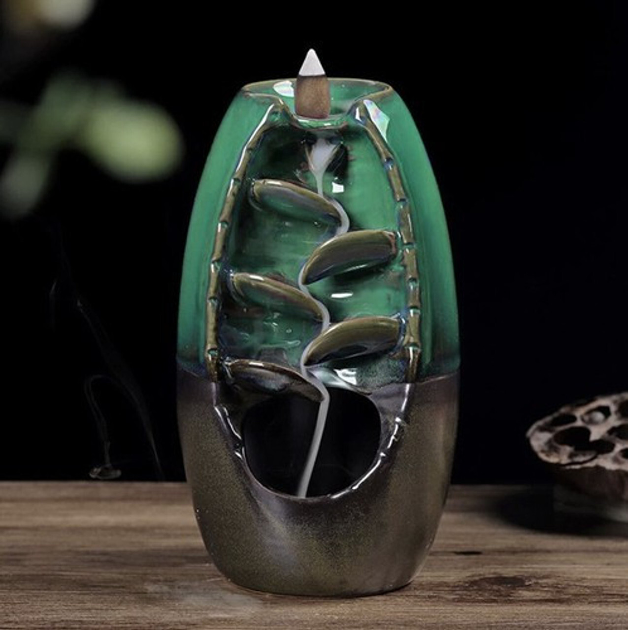 Mirisni kamin vodopad Ruhhy 22655 – keramički backflow s povratnim dimom Keramički mirisni kamin (backflow) u zeleno-grafitnoj boji na drvenoj podlozi; dim se slijeva niz pet ispupčenja i stvara efekt vodopada — za aromaterapiju i opuštanje u domu ili uredu.