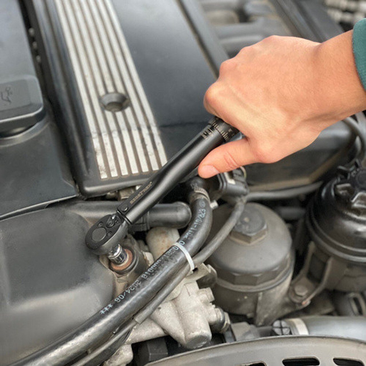 Ruka zateže vijak na motoru automobila crnim dinamometarskim (moment) ključem s račnom; precizno podešavanje momenta za auto-servis, mehaniku i DIY održavanje.