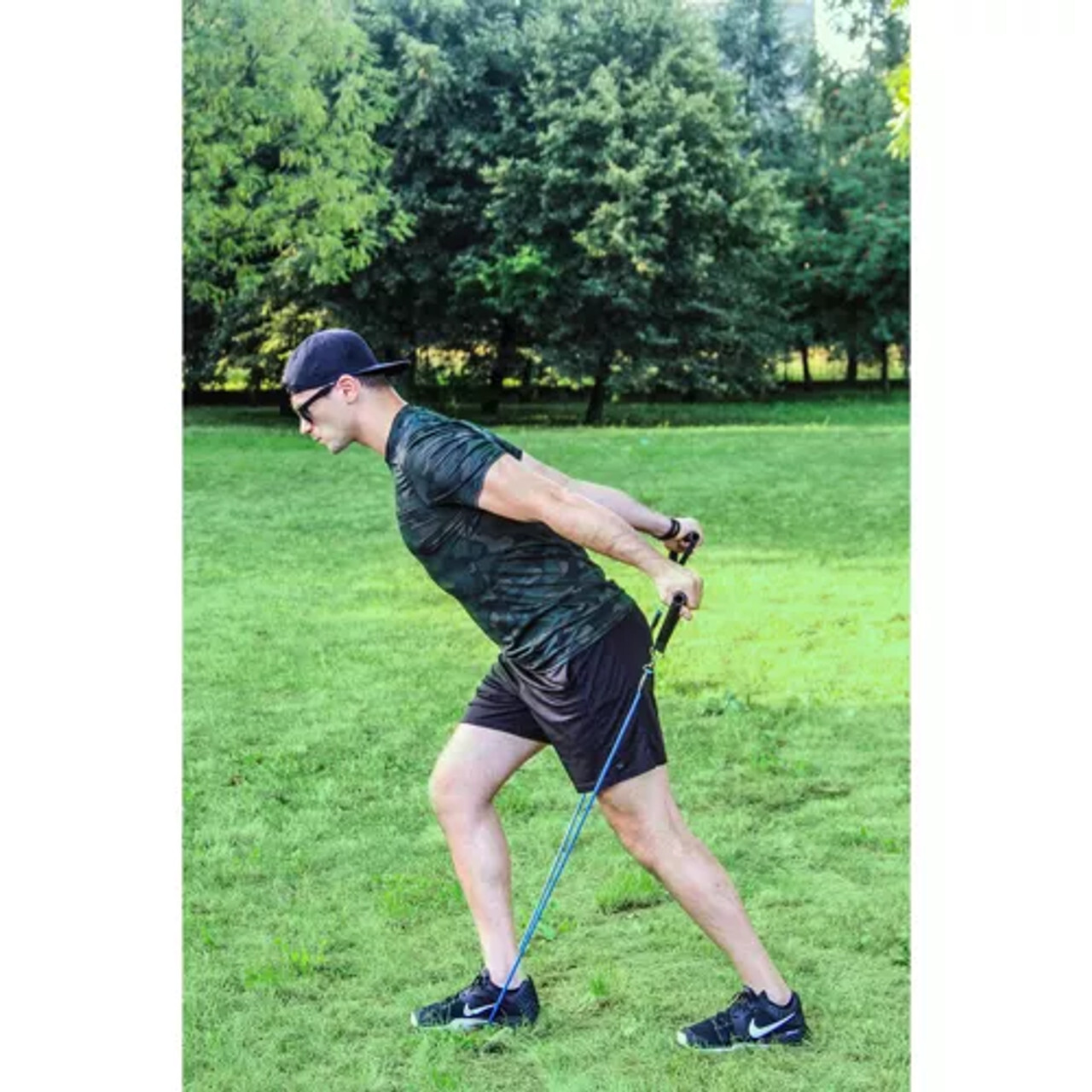 Muškarac u iskoraku izvodi triceps ekstenziju s elastičnom trakom pričvršćenom pod stopalom; neutralna leđa, potisak unatrag kroz ručke. Primjer funkcionalnog treninga s trakama u parku/kući za jačanje ruku i gornjeg dijela tijela.