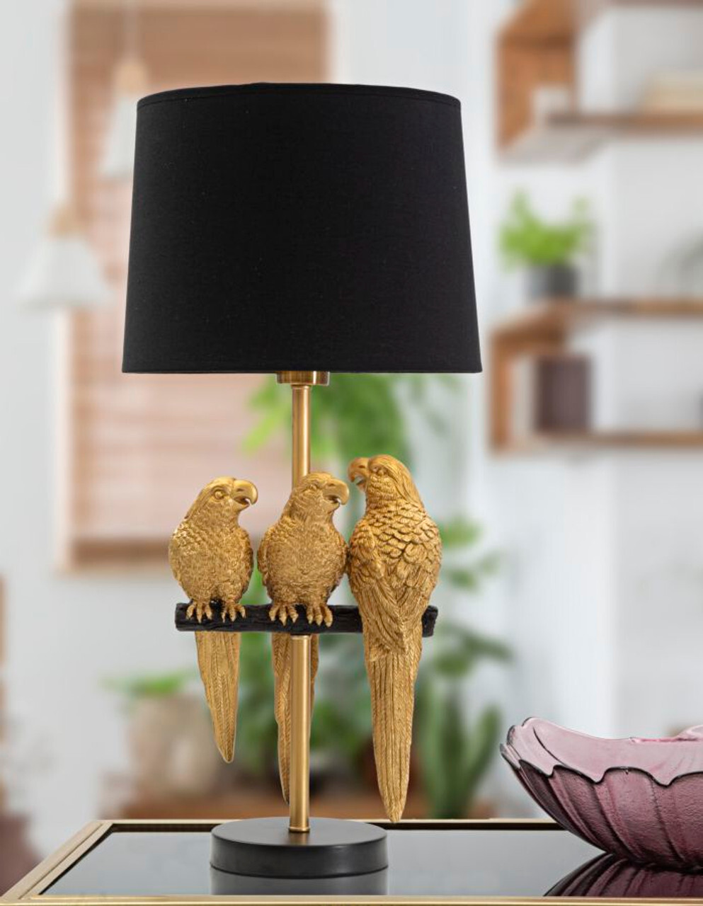 Stolna lampa s crnim sjenilom i bazom u obliku tri zlatna papagaja na grani, u modernom interijeru.